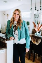 blonde real estate agent standing in a kitchen wearing a turquoise fringe jacket